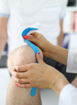 Doctor glue kinesio tape to man on his knee closeup. Injuries in modern sport concept